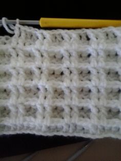 a white crocheted dishcloth with a yellow pen on the side and a black background