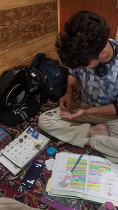 a young man sitting on the floor in front of books and backpacks, reading