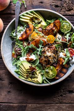 a salad with chicken, avocado and tomatoes in a bowl on a wooden table