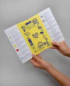 a person holding up a yellow brochure with various things drawn on the pages