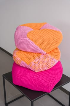 three knitted cushions stacked on top of each other in different colors and sizes, sitting on a black table