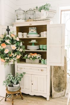 an old china cabinet with flowers and plates on it