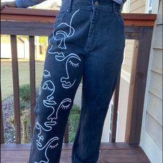 a woman standing on top of a wooden deck wearing jeans with faces drawn on them