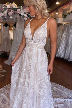 a woman in a white wedding dress standing on a table with dresses hanging up behind her