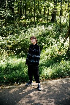 a man standing on the side of a road in front of some trees and bushes