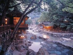 a river running through a lush green forest next to wooden buildings with lit up windows