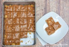 a pan filled with peanut butter squares on top of a wooden table next to a white plate