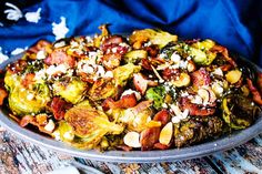 a plate full of brussel sprouts with bacon and pine nuts on top