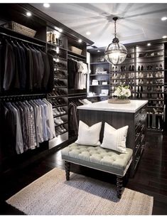 a walk - in closet with lots of clothes on shelves and a bench next to it