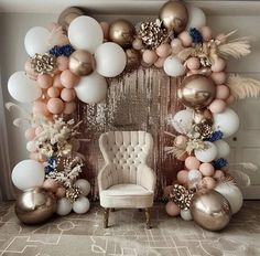 a chair sitting in front of a large balloon arch with balloons and feathers on it