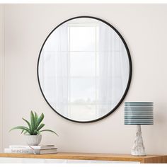 a round mirror on the wall above a table with a lamp and potted plant