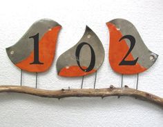 three metal birds sitting on top of a tree branch with numbers painted on the sides