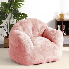 a pink bean bag chair sitting on top of a carpeted floor next to a potted plant