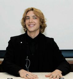 a smiling man sitting at a table with his hands folded out in front of him