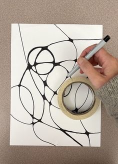 a person is holding a tape and drawing on a piece of paper with black ink