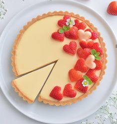 a cheesecake topped with strawberries on top of a white plate next to flowers