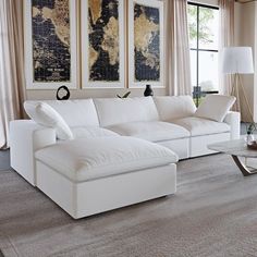 a living room filled with white furniture and large paintings on the wall above it's windows