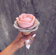 a hand holding an ice cream cone with pink frosting on top and a flower in the middle