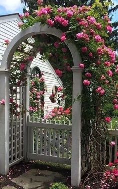 a white picket fence with pink flowers growing on it and an arch in the middle