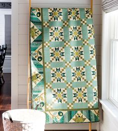 a green and white quilt sitting on top of a wooden stand next to a window