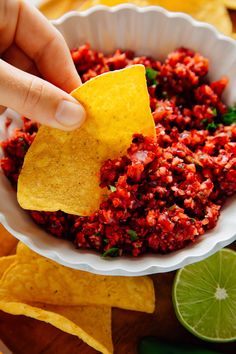 a person dipping a tortilla chip into a bowl filled with salsa and limes