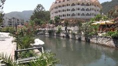 a river running through a lush green park next to a tall white building with arched windows