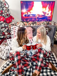 two women are sitting on the floor with plaid pajamas and holding mugs in their hands