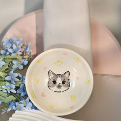 a plate with a cat face on it next to blue flowers and a white napkin