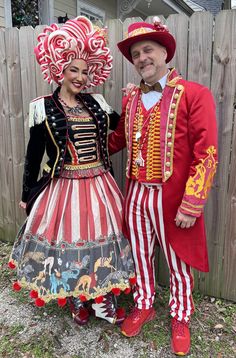 a man and woman dressed in costume standing next to each other near a wooden fence