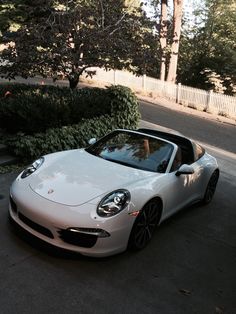 a white sports car parked on the side of the road next to some bushes and trees