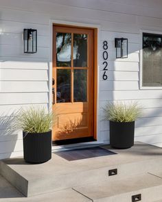 two black planters on the front steps of a white house with brown door and windows