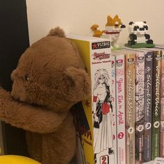 a brown teddy bear sitting on top of a book shelf next to a pile of books