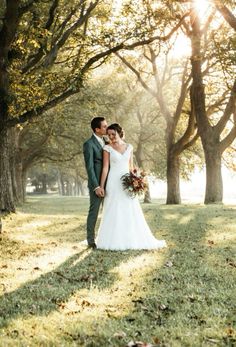 a bride and groom standing in the grass under trees