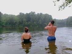 two people are sitting in the water looking at something on the other side of the lake