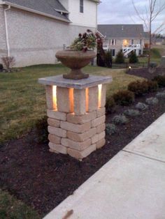 a light that is on top of a brick pillar in front of some grass and bushes