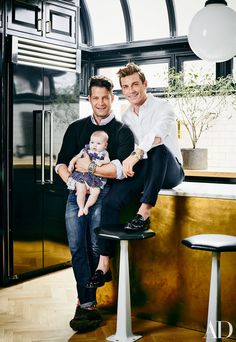 two men and a baby are sitting on a stool in front of a kitchen counter