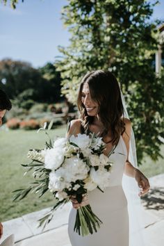 a woman in a wedding dress holding a bouquet and smiling at another woman who is standing next to her