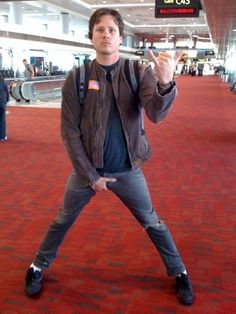 a man standing in the middle of an airport with his hand up and pointing at something