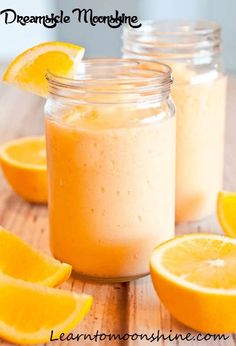 two mason jars filled with orange smoothie on top of a wooden table next to sliced lemons