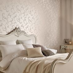 a white bed sitting in a bedroom next to a wallpapered headboard and night stand