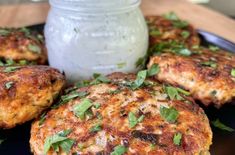 several crab cakes on a black plate with a jar of ranch dressing in the background