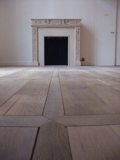 an empty room with wooden floors and a fireplace in the center, surrounded by white walls