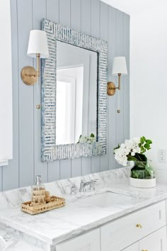 a bathroom with blue and white walls, marble countertops and gold accents on the mirror