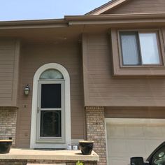 a brown house with two cars parked in front of it and the door is open