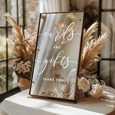 a card and gifts sign sitting on top of a table next to some dried flowers