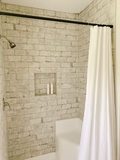 a white shower curtain in a bathroom next to a toilet and bathtub with a brick wall behind it