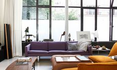 a living room filled with lots of furniture next to tall windows and floor to ceiling windows