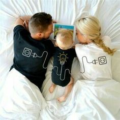 a man and woman laying in bed reading a book to a child with an electric lightbulb on their shirt