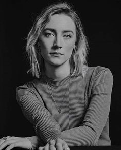 a black and white photo of a woman leaning on a table with her arms crossed