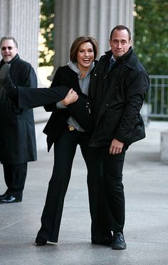 a man and woman standing next to each other in front of columns with their arms around each other